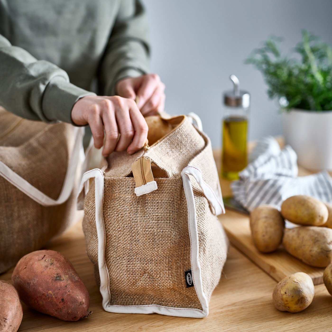 A person unzips a GULLRISMOTT food storage bag set on a kitchen worktop. Potatoes and sweet potatoes are on the worktop.