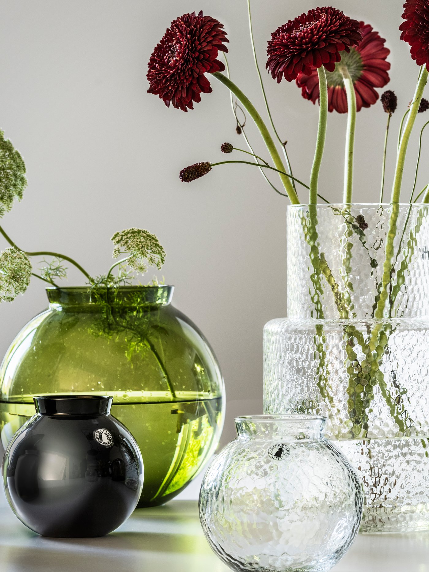 Glass KONSTFULL vases with red flowers in it on a table.