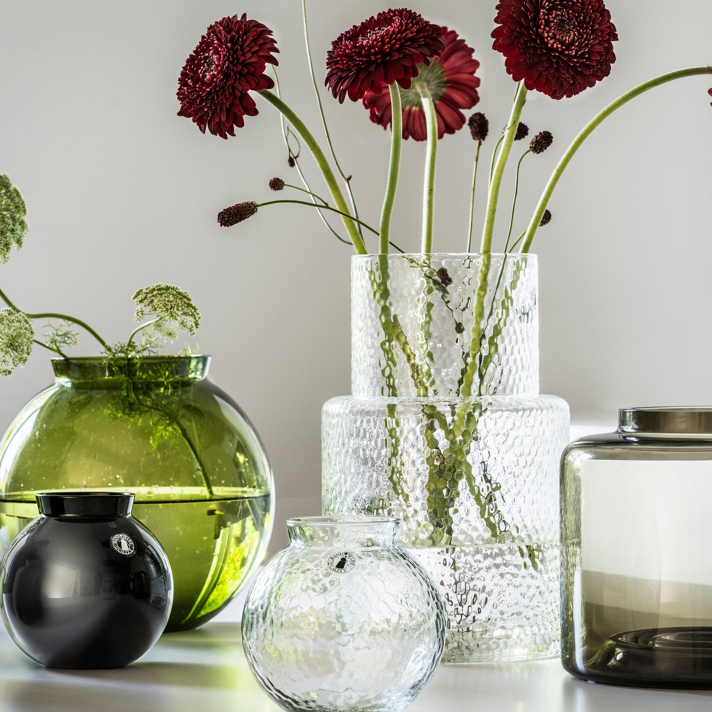 KONSTFULL vases in glass with flowers on a white table in bright room.