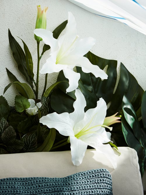 ベージュの屋外用ソファクッションと立てかけられたブルーの枕の後ろにあるSMYCKA/スミッカ 造花 白百合のクローズアップです