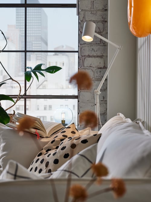 Bedroom with a white floor reading lamp with adjustable head and arm placed next to a 2-seat sofa and a table lamp.