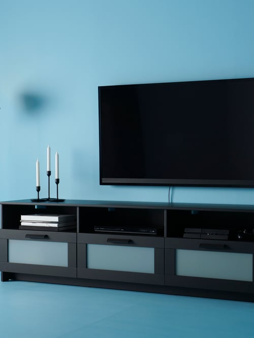 Living room with a blue wall, featuring a black tv bench with a wide screen TV and a three black candlesticks.
