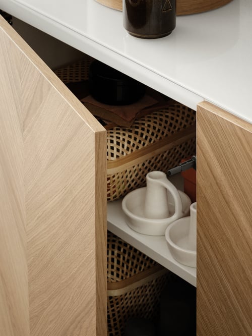 A BESTÅ cabinet with one door slightly open, showing candle holders and storage baskets on the shelves.