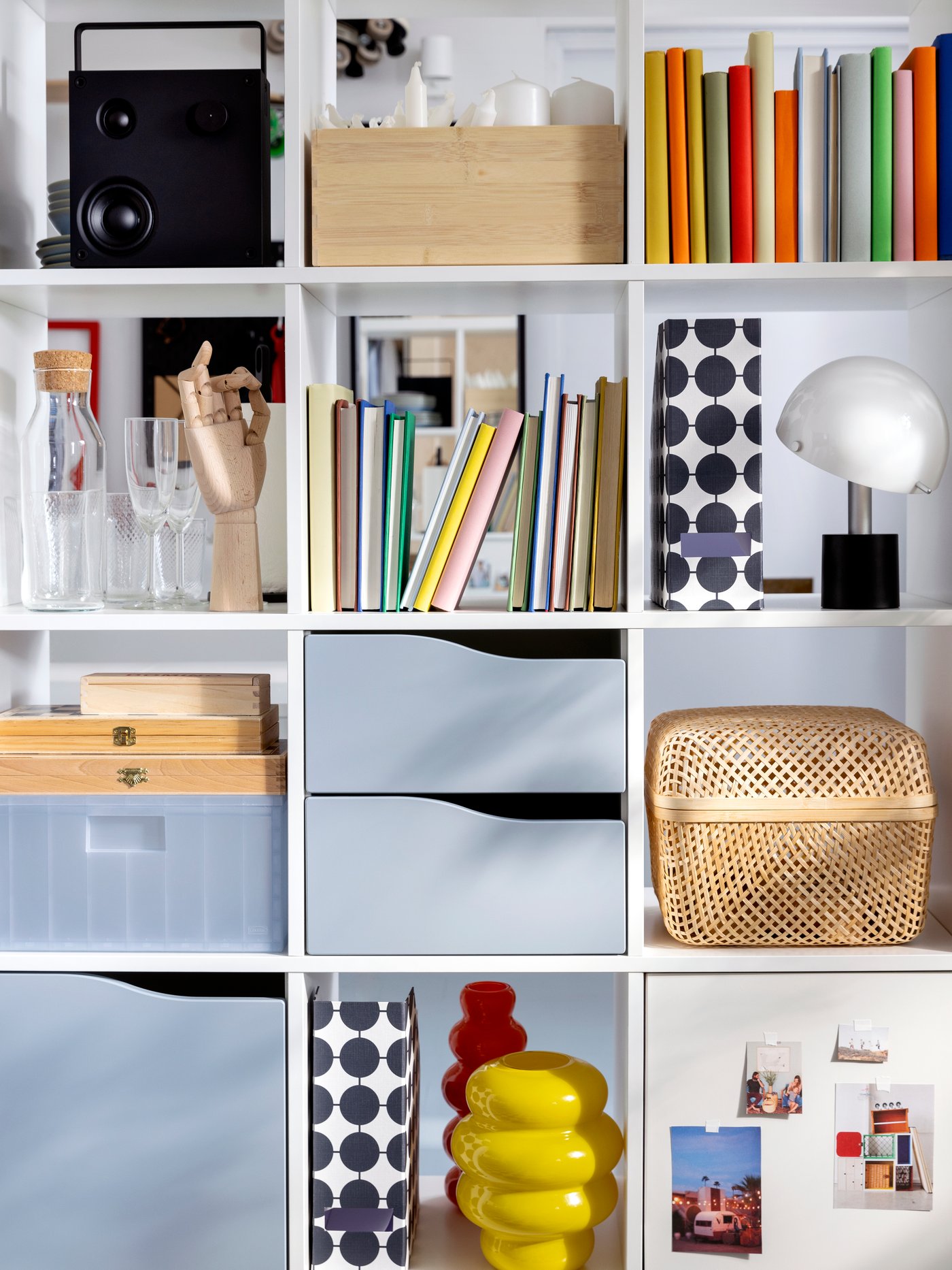 Objects including a VAPPEBY Bluetooth speaker and a SMARRA box with lid stand on the shelves of a white KALLAX shelving unit.