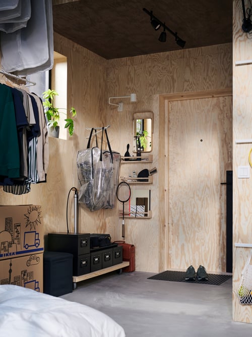 Hallway with storage bag, black storage boxes with lids, black footstool with storage space, wall lamp with swinging arm.
