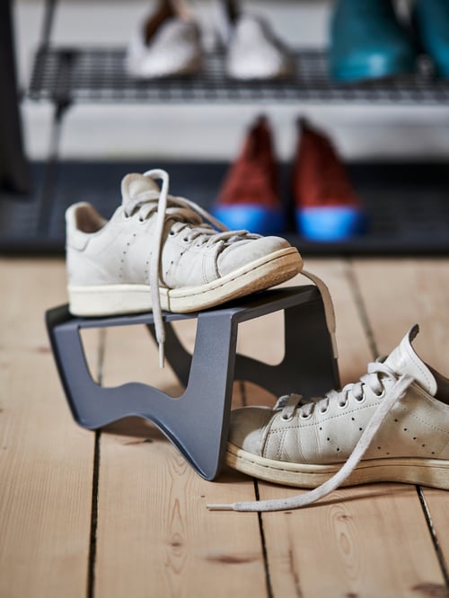 A wooden-floor hallway with a MURVEL shoe organiser holding one sneaker, its mate placed halfway into the hollow beneath.