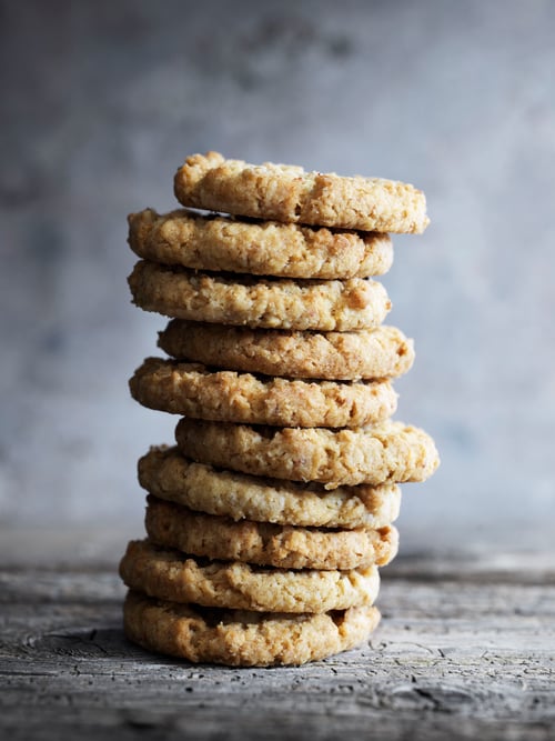 Dining room focus of multiple crunchy biscuits with fine crumbs of almond and a touch of caramel placed on a grey surface.