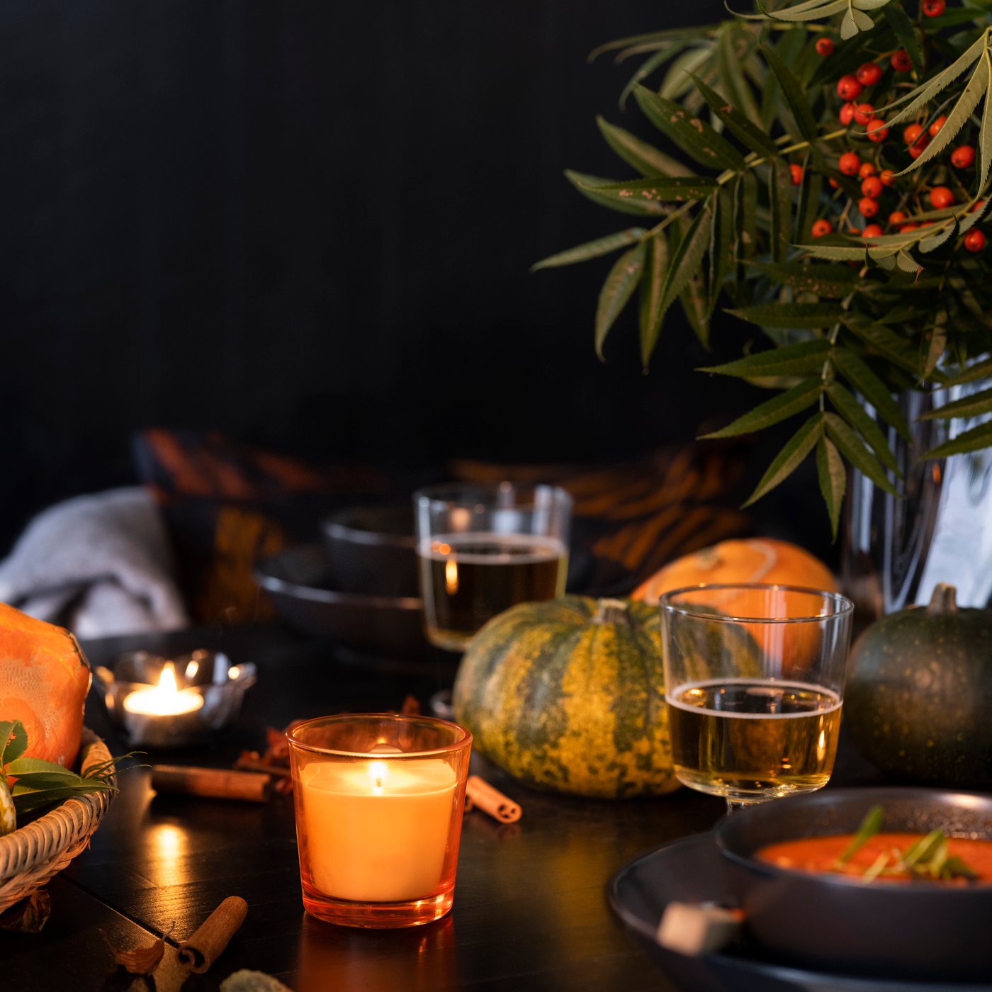 Set di 3 zucche decorative su una tavola con bicchieri e candele accese.