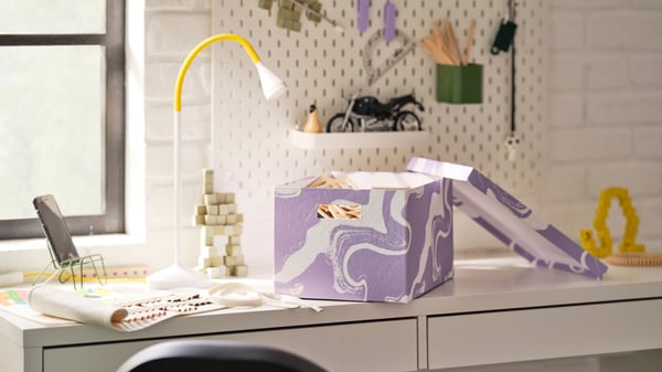 A patterned/lilac white TJENA storage box with lid in the childrens room