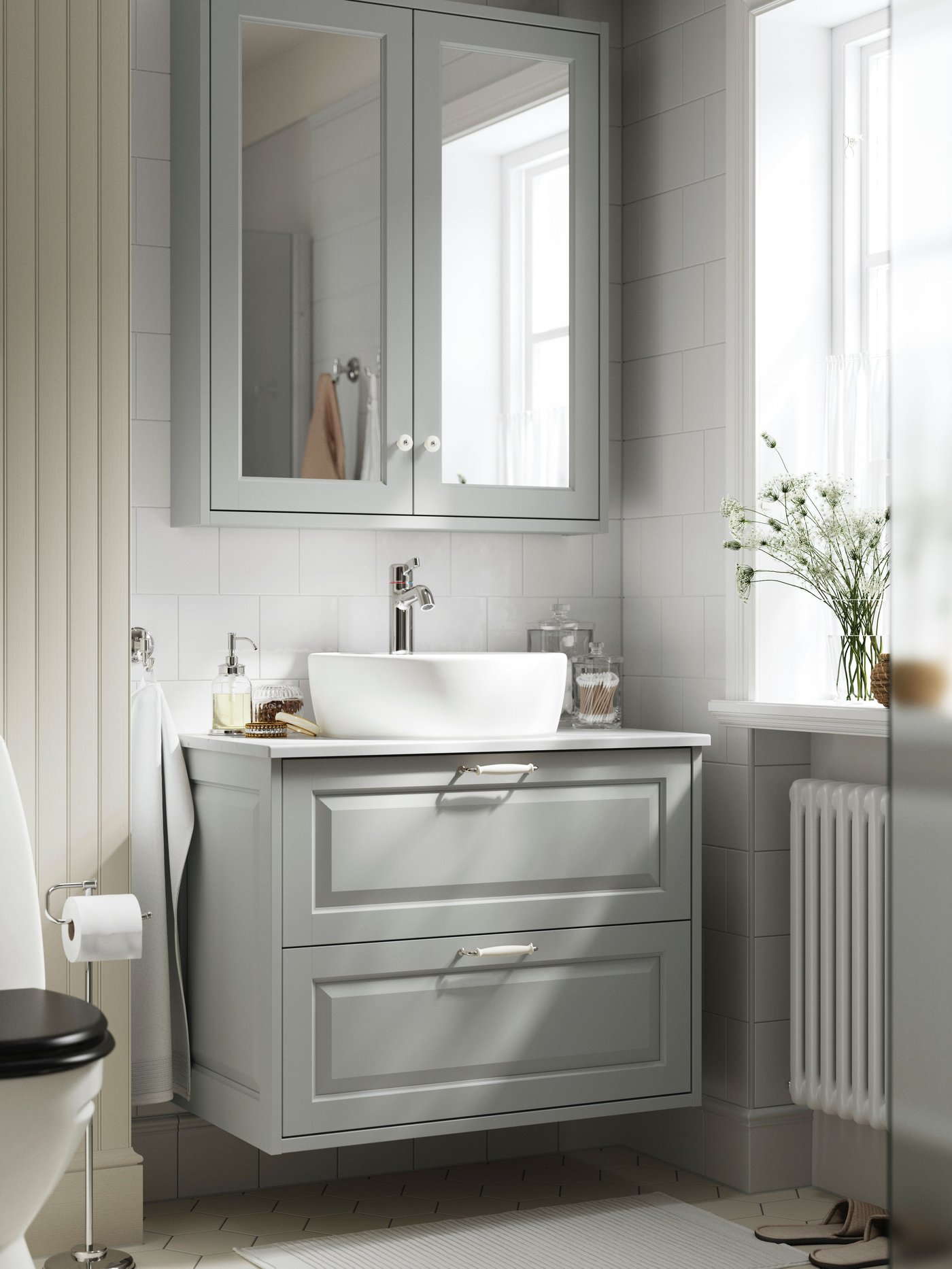 A white-tiled bathroom has a light-grey TÄNNFORSEN wash-stand with two drawers and a mirror cabinet with two doors above it.