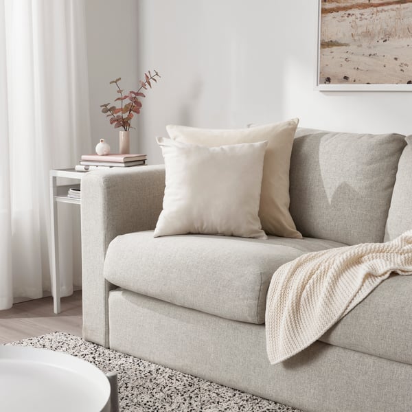 Canapé en tissu beige avec des coussins et une couverture blanche.