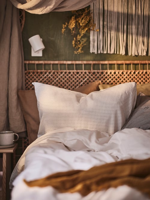 Close up of a bedroom setting with a ÄNGSLILJA duvet cover and pillowcase set placed in a VEVELSTAD tolkning rattan bed.