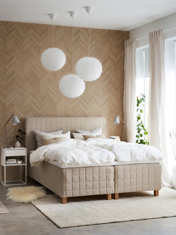 Vaalea makuuhuone, jonka keskellä on IKEA-jenkkisänky. Sängyn päällä on valkoiset petivaatteet ja yläpuolella kolme valkoista valaisinta.