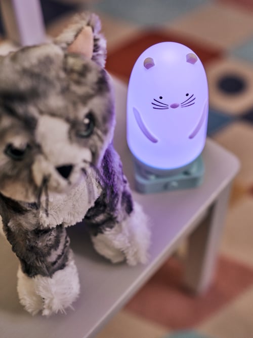 Stuhl mit einem SPIKEN LED-Nachtlicht neben einem LILLEPLUTT Stofftier in Katzenform.