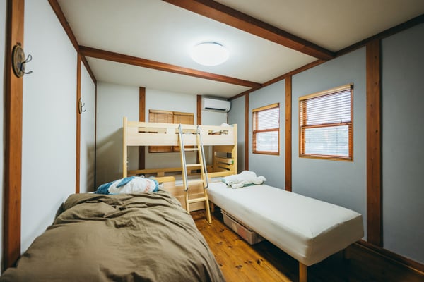 木目調の梁と窓枠がある部屋に、2台のベッドと1台の二段ベッドが置かれている。