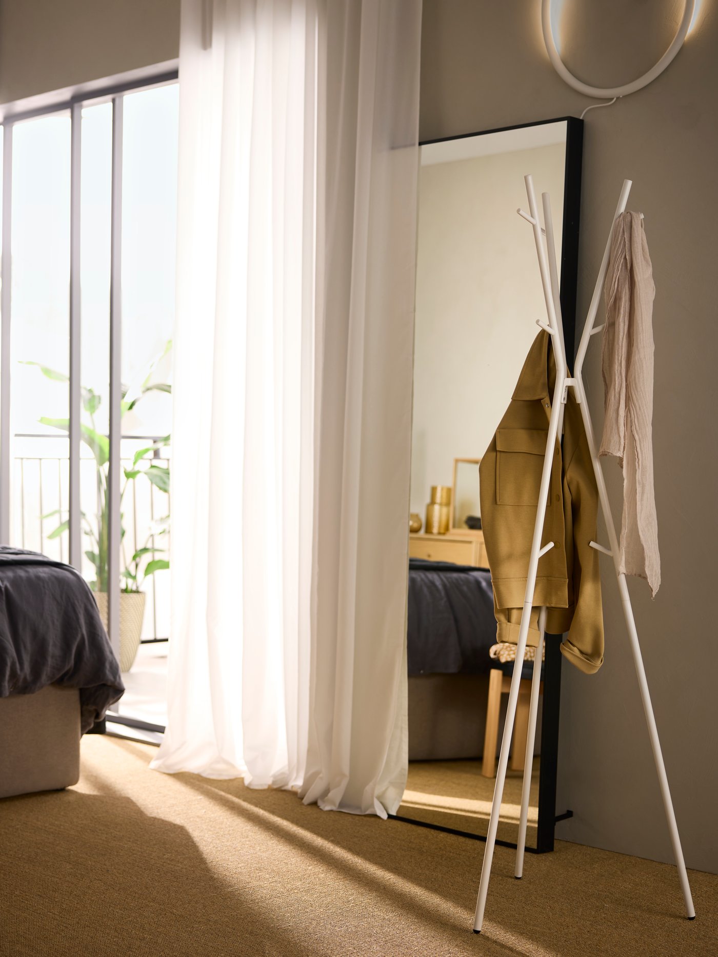 A white EKRAR hat/coat stand holding a couple of items of clothing by a window with a sheer white ROSENROBINIA curtain on it.
