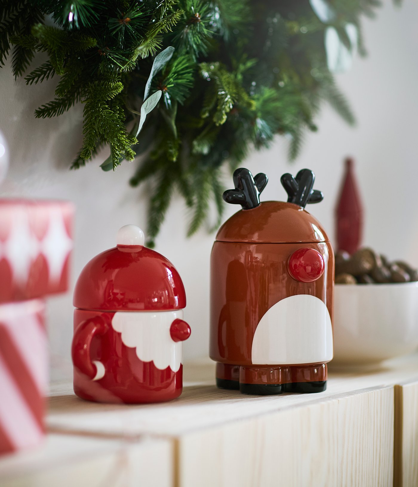 Bonbonnière avec couvercle VINTERFINT en céramique rouge en forme de Père Noël à côté d’une bonbonnière avec couvercle VINTERFINT brune en forme de renne.