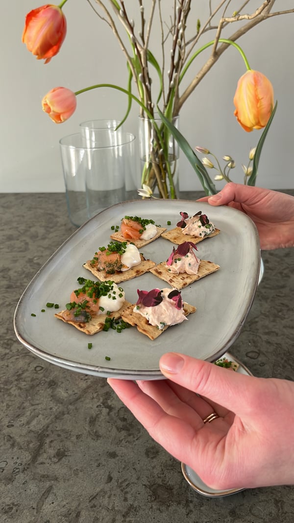 Ett GLADELIG fat med laxsnittar på hålls upp och i bakgrunden syns vaser med tulpaner i.