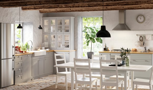 Una cucina LERHYTTAN grigio chiaro con credenza, sedie bianche, tavolo, cassetti e scompartimento. Il tavolo è illuminato con una lampada a sospensione SKURUP.