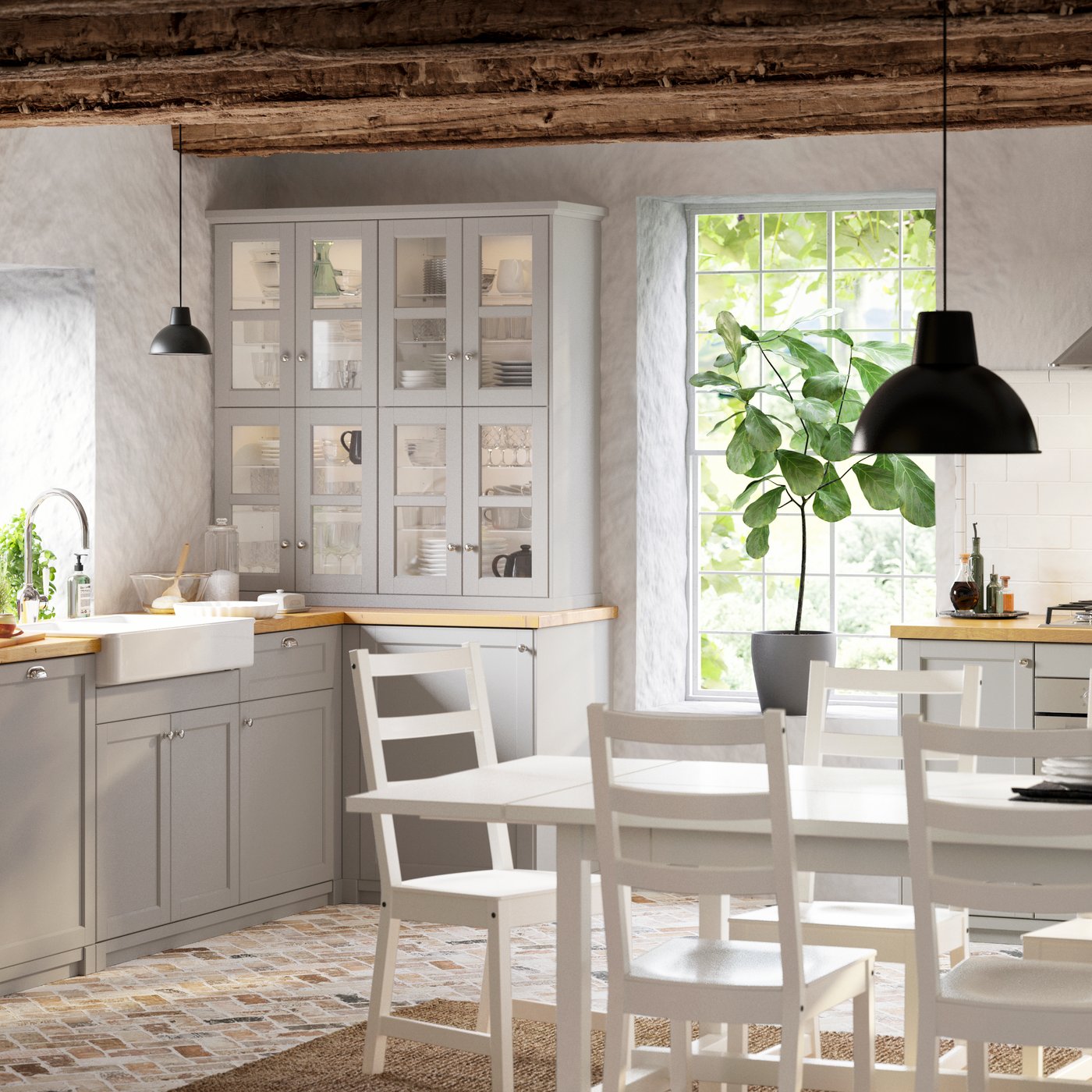 Una cucina LERHYTTAN grigio chiaro con credenza, sedie bianche, tavolo, cassetti e scompartimento. Il tavolo è illuminato con una lampada a sospensione SKURUP.