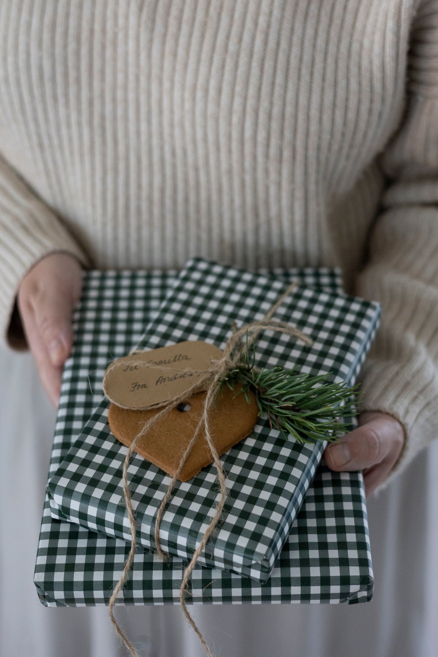 To gaver pakket ind i grønt og hvidt ternet gavepapir med et brunkagehjerte og en grankvist på.