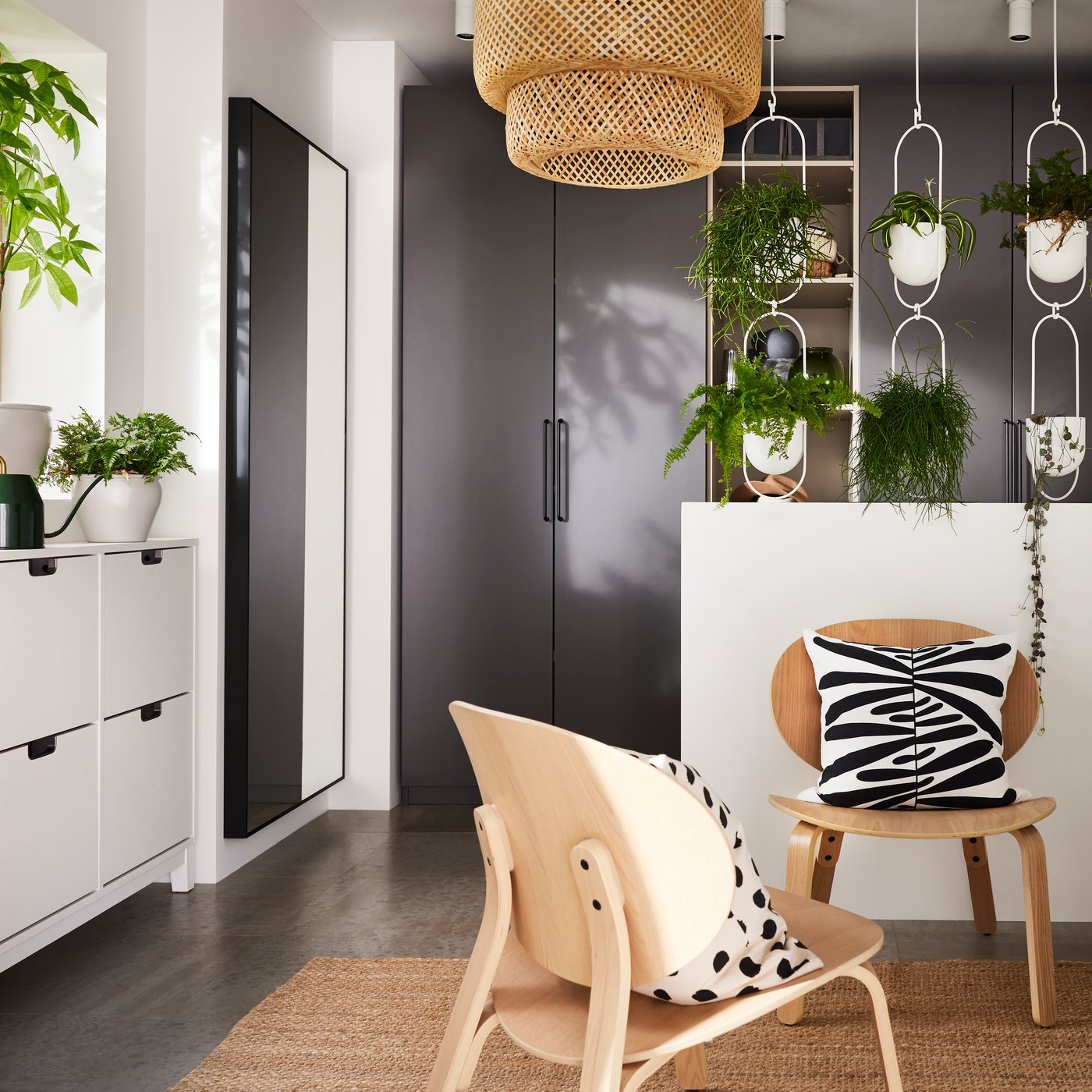 Un ingresso con una combinazione di guardaroba PAX grigi, una lampada a sospensione SINNERLIG in bambù e una serie di scarpiere STÄLL allineate sotto al davanzale di una finestra con varie piante in vaso.