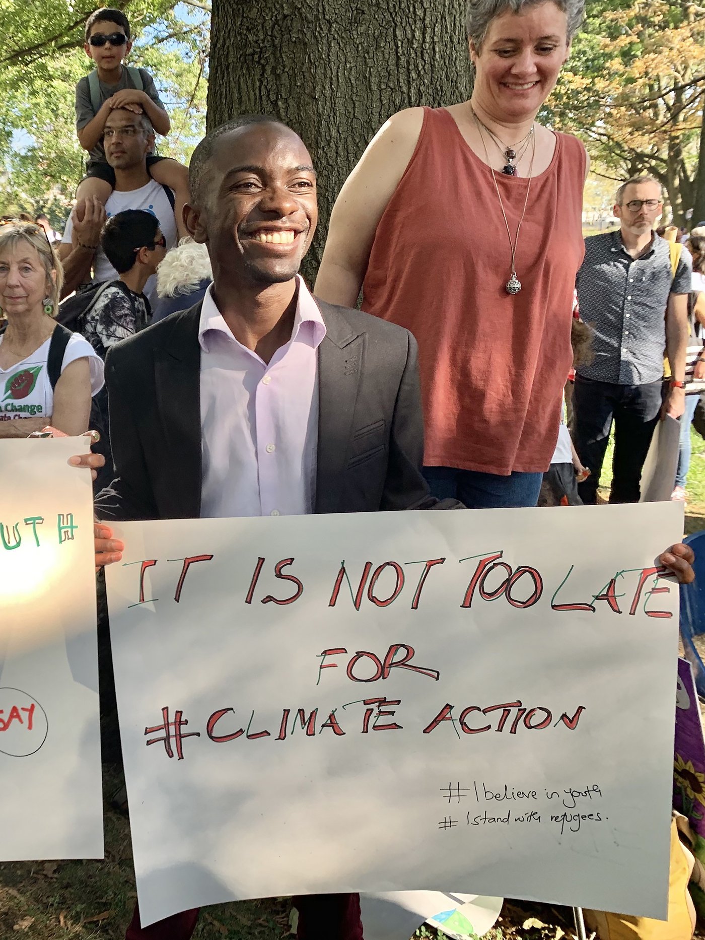 Barthelemy Mwanza, Geflüchteter aus dem Kongo, hält ein Plakat hoch, auf dem ein Slogan über den Klimawandel steht, und lächelt in die Kamera.