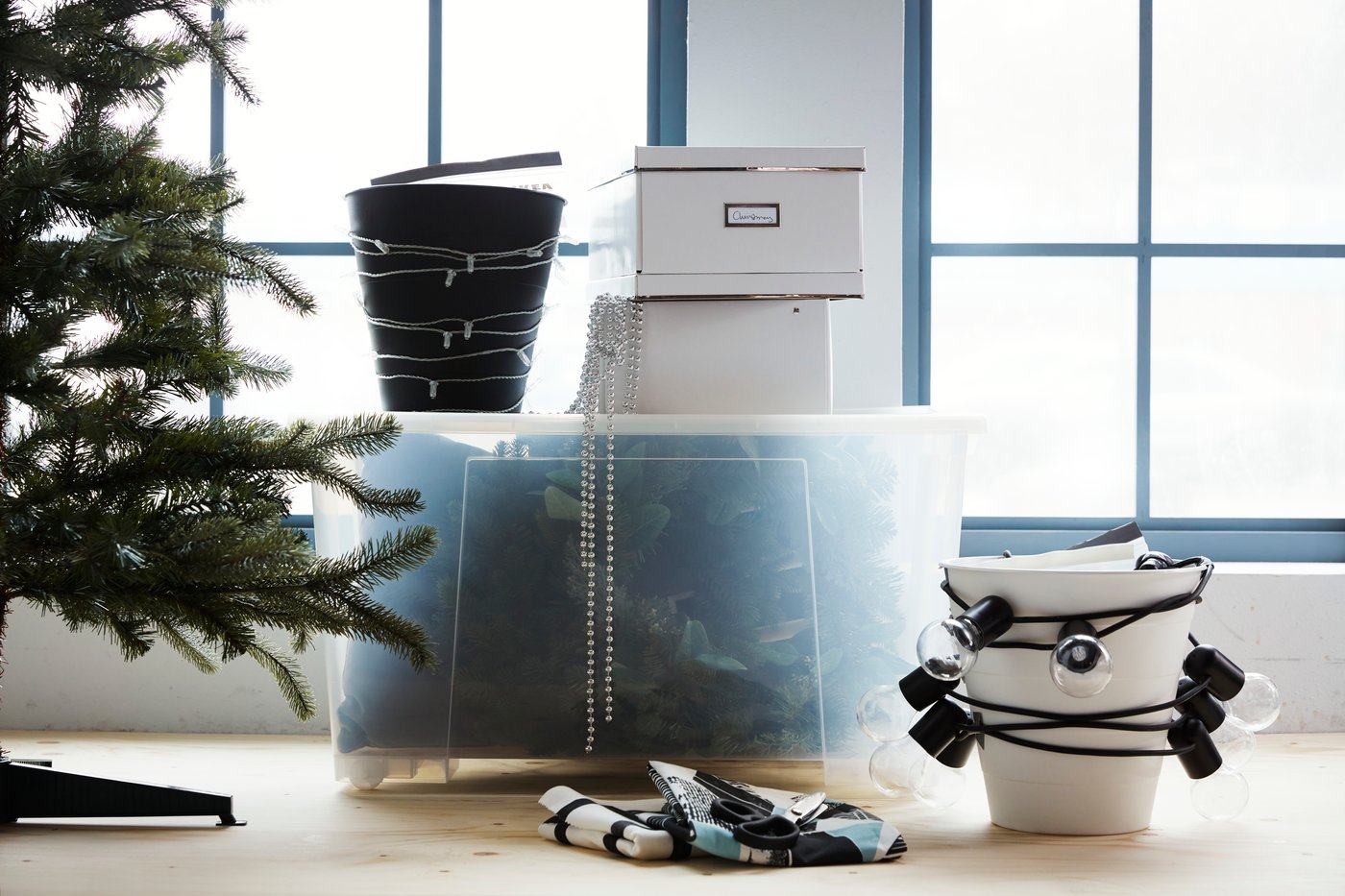Eine dursichtige Box mit Weihnachtsdeko, eine Eimer mit einer Lichterkette und ein Teil von einem Weihnachtsbaum.