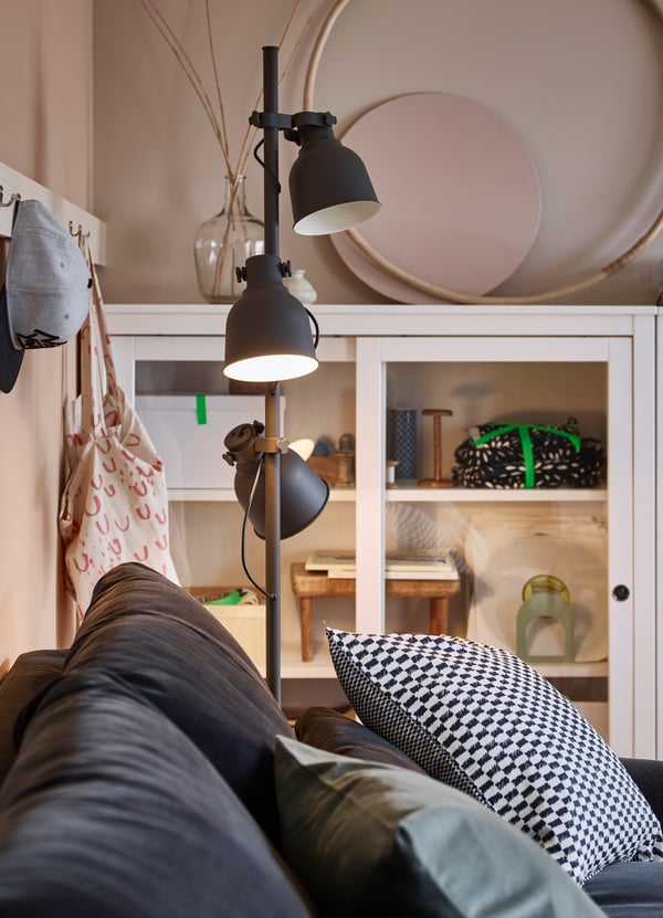 Una lámpara de pie HEKTAR gris oscuro con 3 focos iluminando un sofá de una sala.