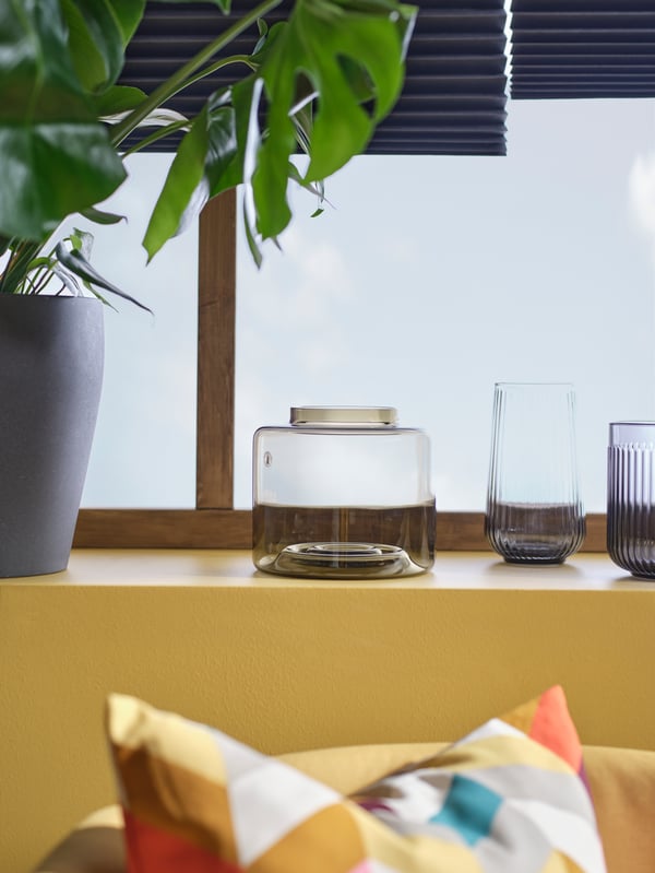 Smoked and rippled glass vases are lined up with a monstera plant on the windowsill of a modern deco style room.