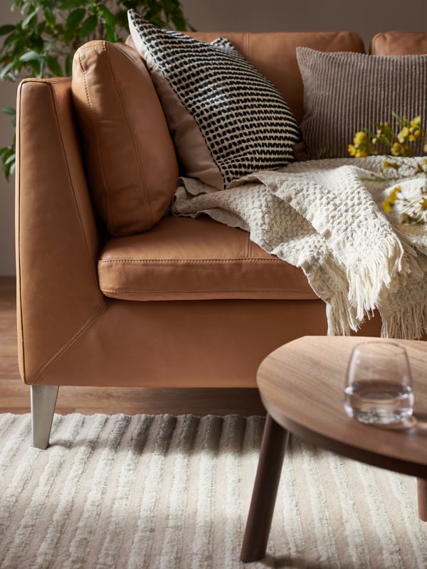 Et mysigt vardagsrum med brun skinnsoffa med prydnadskuddar och filt i beige. 