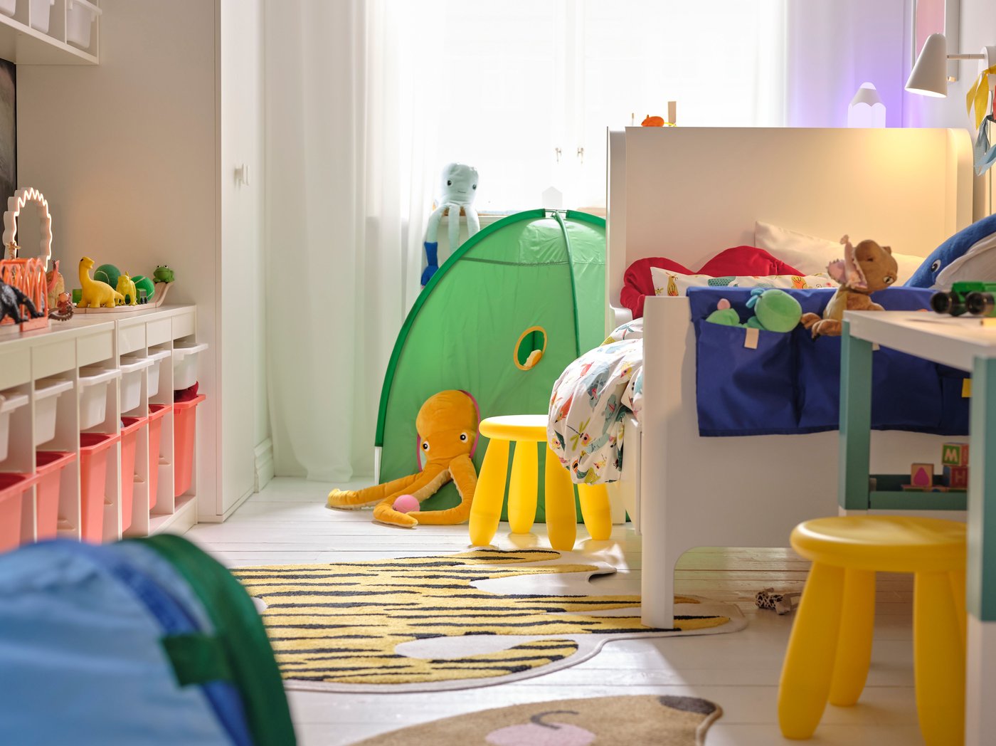 Una taula extensible BUSUNGE a un costat d'un dormitori petit amb un tamboret MAMMUT groc al costat i una tenda de campanya infantil verda al darrere.
