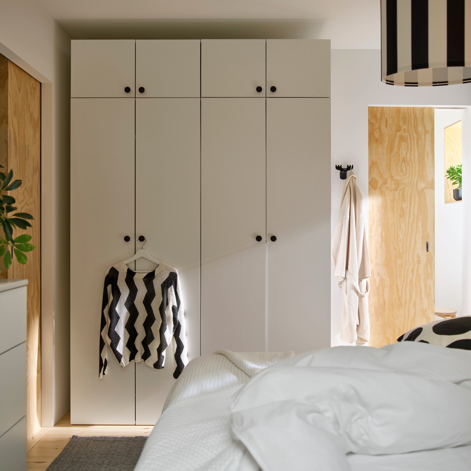 LASTARE wardrobe combination in white with closed doors and a striped shirt hanging in a bright bedroom.