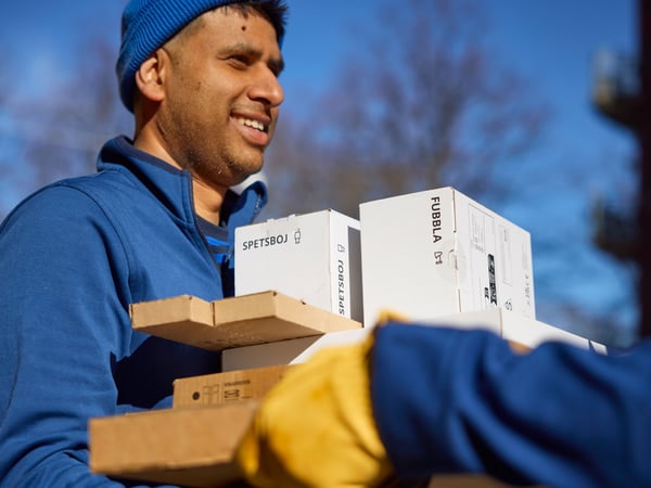 Une personne en uniforme bleu transporte à l'extérieur des cartons à monter et des colis empilés lors de la livraison d'une commande à domicile.