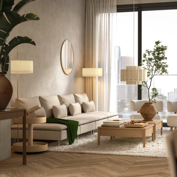 A modern apartment’s living room with big windows has a long, beige SÖDERHAMN modular sofa by two oak veneer coffee tables.