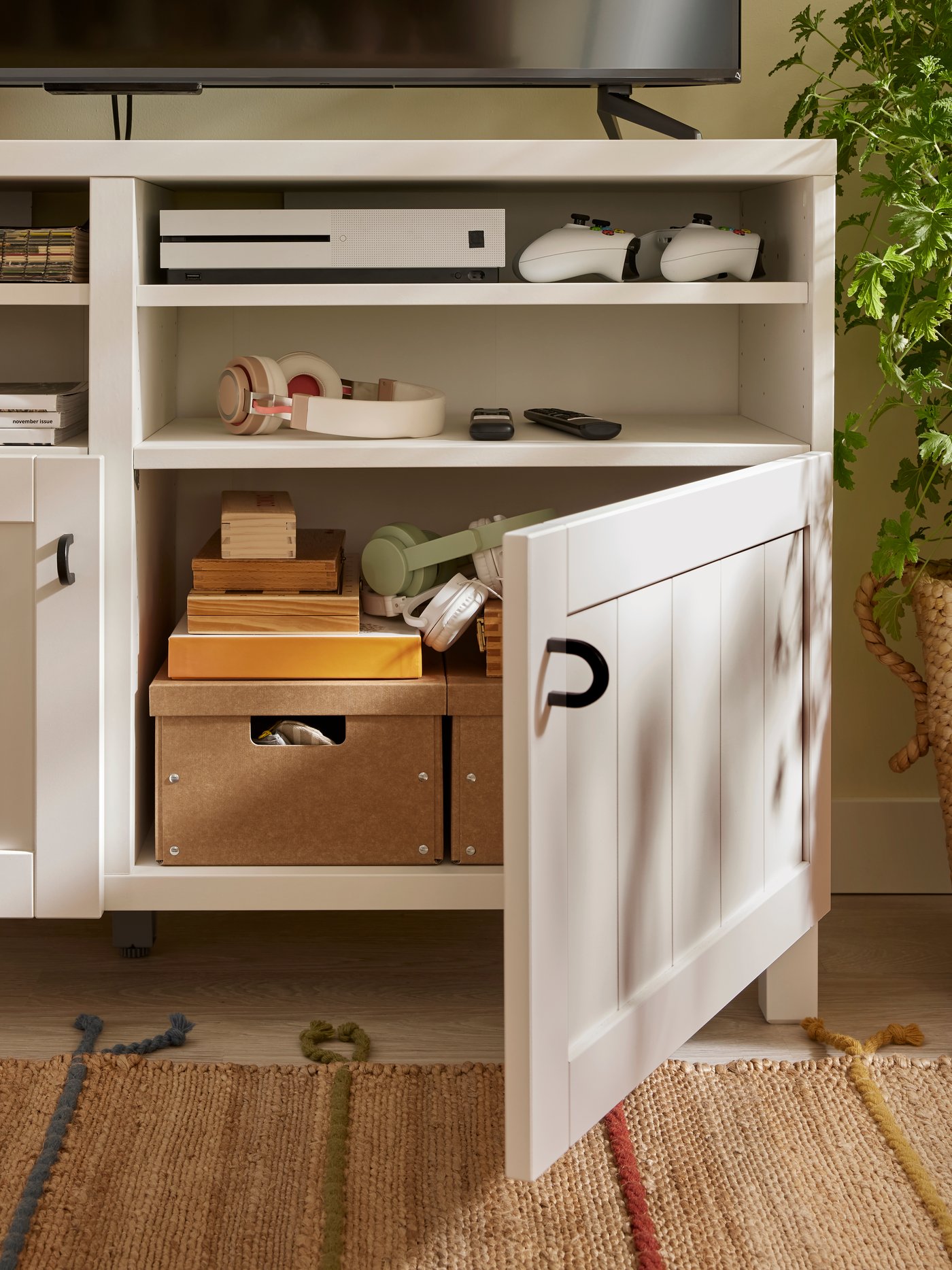 Pojemniki GÄRDESGÅRD z pokrywkami ustawione na półce białej szafki pod telewizor BESTÅ z drzwiami PIPMAKARE. Jedne z drzwi są otwarte.