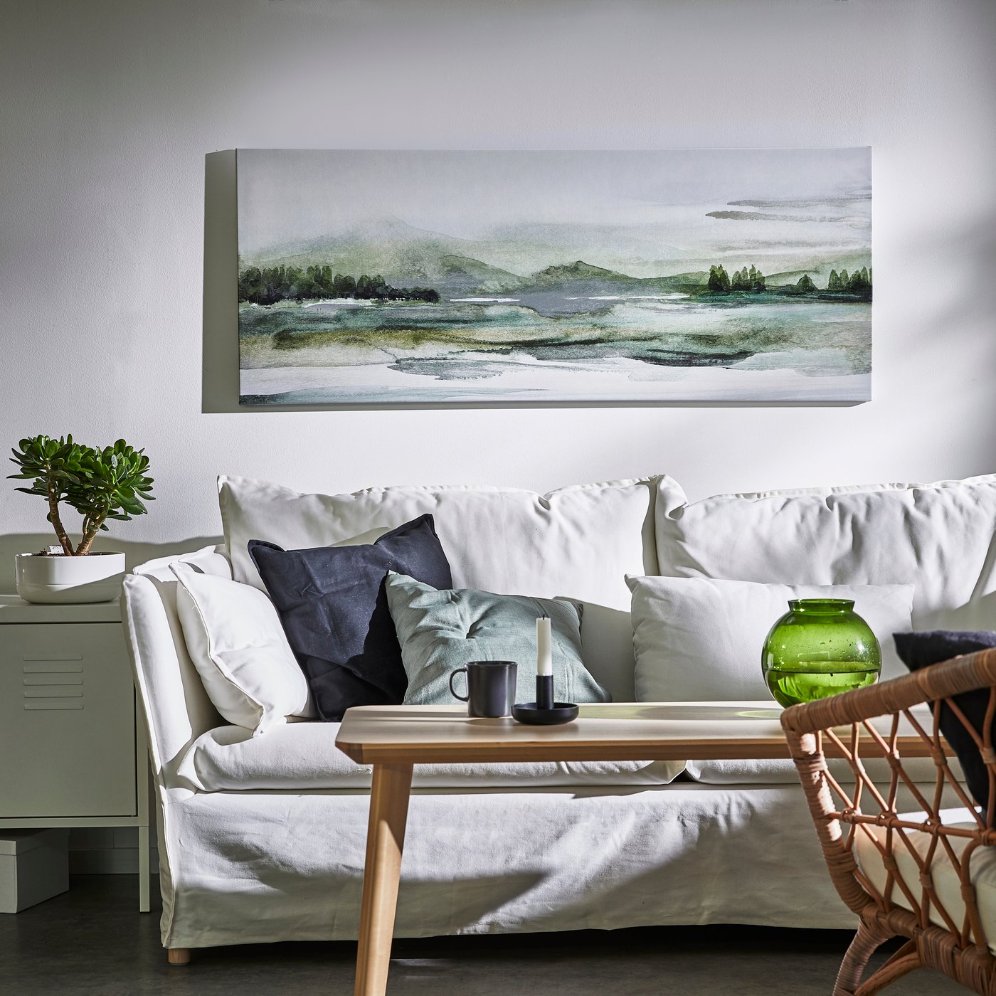 Smal tavla med naturmotiv på vägg ovanför soffa. 