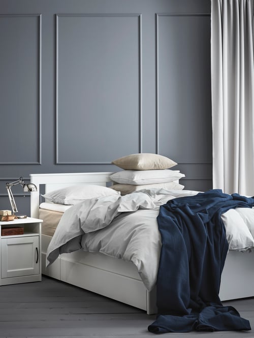 Bedroom with white bed frame, bedside table, duvet cover, pillowcases, cushion covers, bedspread, work lamp, cushion cover.