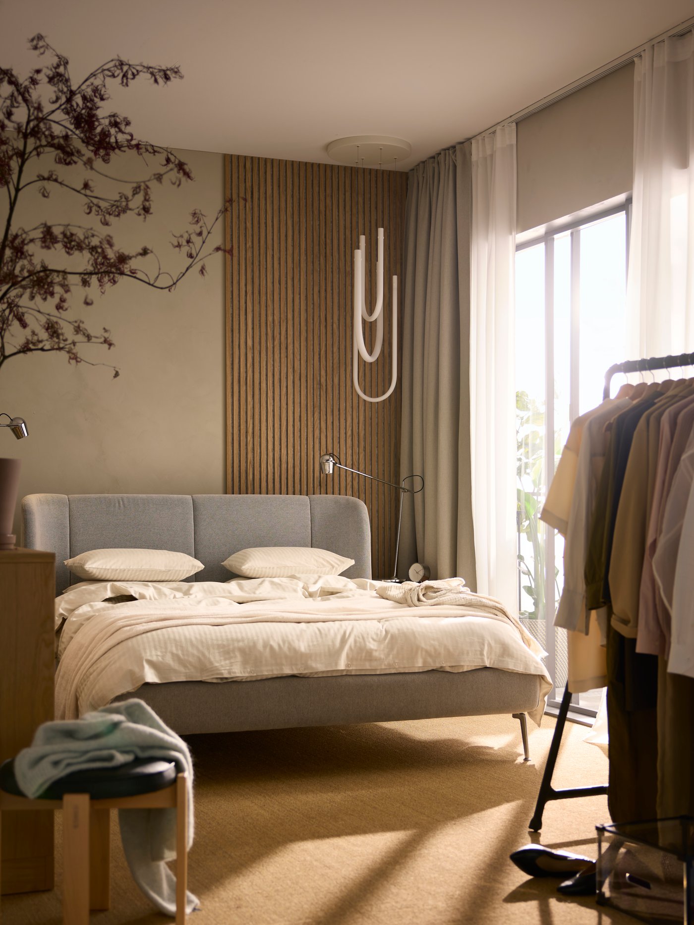 A Tallmyra white/black TUFJORD upholstered bed covered in light beige NATTJASMIN bed linen. A VARMBLIXT LED lamp is above it.