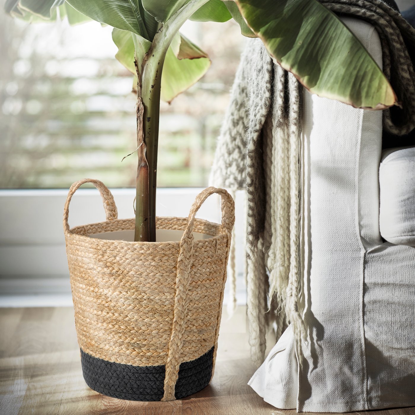 Maceta TÄRNMÅS para interior en color beige y negro, con una planta de interior junto a un sofá.
