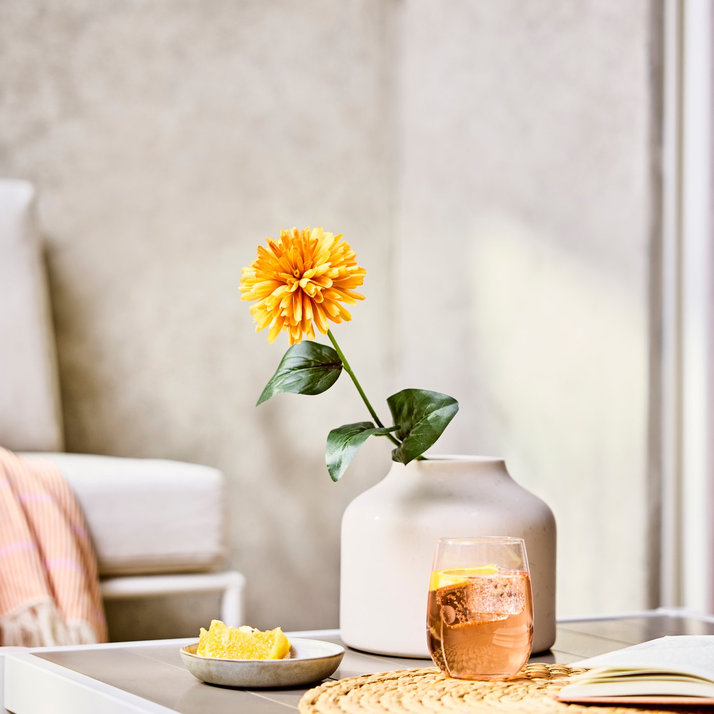 Artificial chrysanthemum stem in a matte vase on a side table beside a candle and bowl.