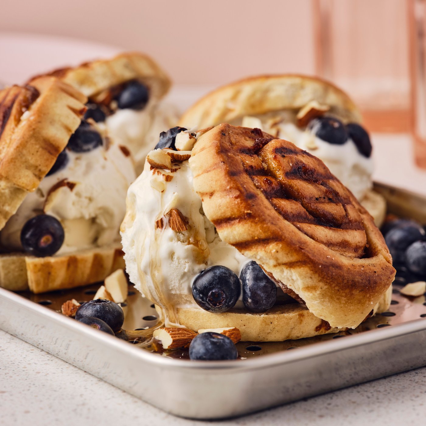 Záběr zblízka na tři grilované skořicové rolky KAFFEREP, zmrzlinu, borůvky a sekané mandle.