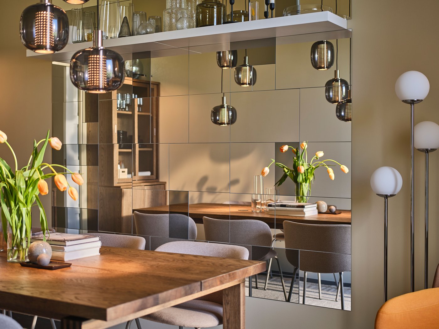 Une grande table MÖRBYLÅNGA trône au centre d’une salle à manger étroite mais raffinée, avec de nombreux miroirs au mur.
