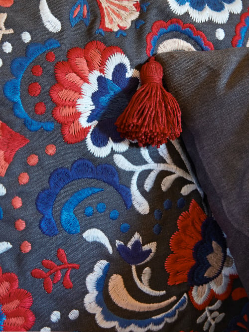 Close-up of SKOGSKORN cushion with a colourful paisley print on a dark background; accented with a red tassel.
