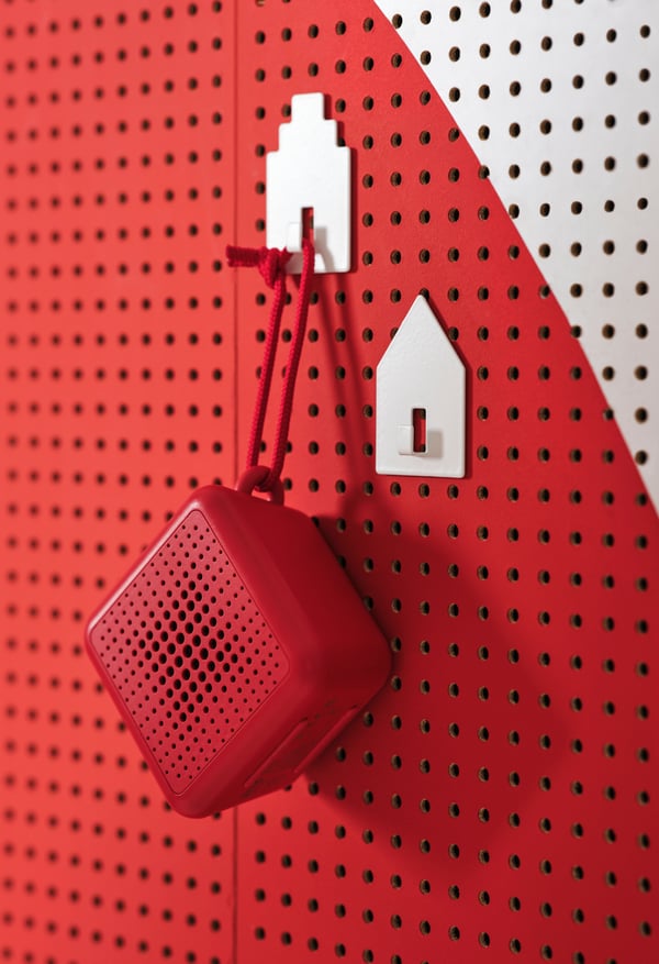 An einer weissen und roten Wand hängt ein roter Bluetooth-Lautsprecher an einer roten Schnur.
