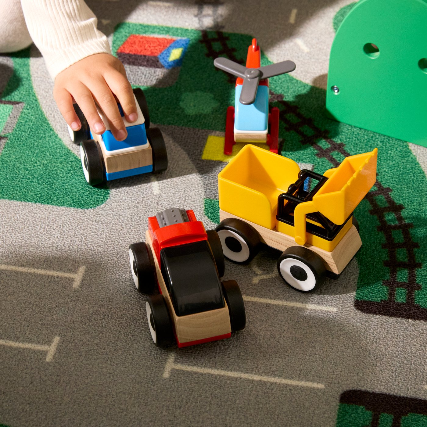 Close-up of a little child’s hand playing with LILLABO toy vehicles and helicopter on the LILLABO rug.