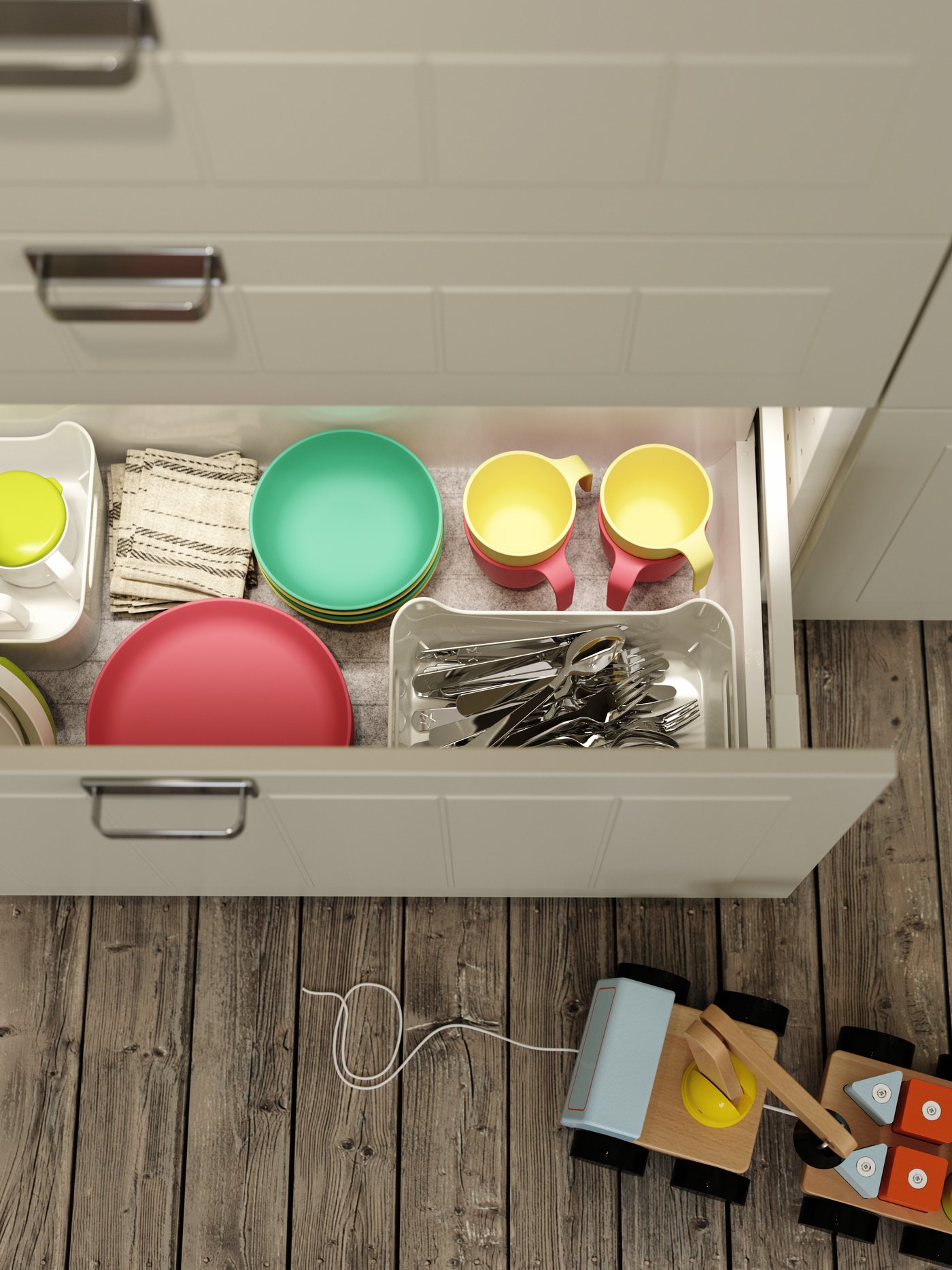 Laci bawah berwarna kuning air ditarik keluar yang menampakkan pinggan mangkuk meja kanak-kanak berwarna merah, hijau dan kuning. Mainan kayu di atas lantai.