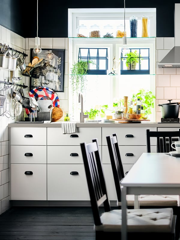 A corner of a black-and-white kitchen with white base cabinets and multiple utensils on rails fitted on a white-tiled wall.