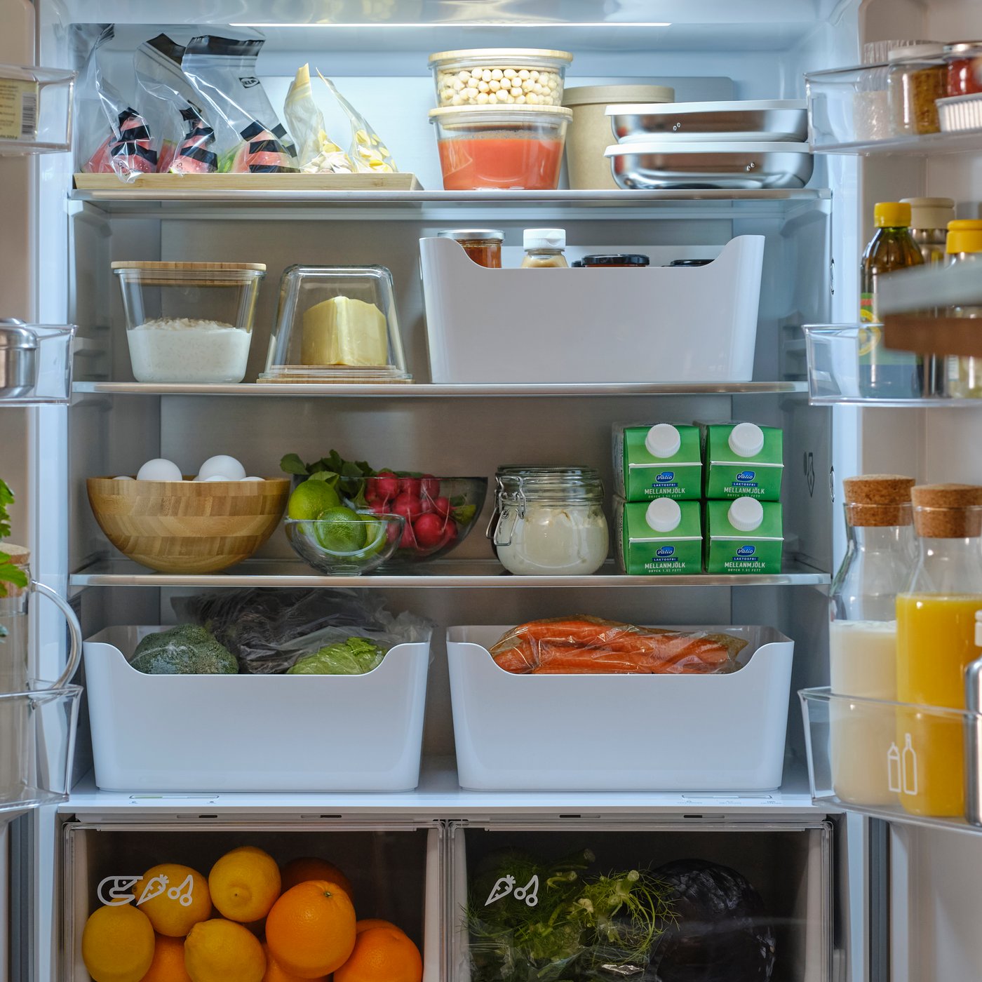 Un frigo con diversi alimenti riposti in contenitori frigo, ciotole,  buste richiudibili ISTAD e bottiglie KORKEN.