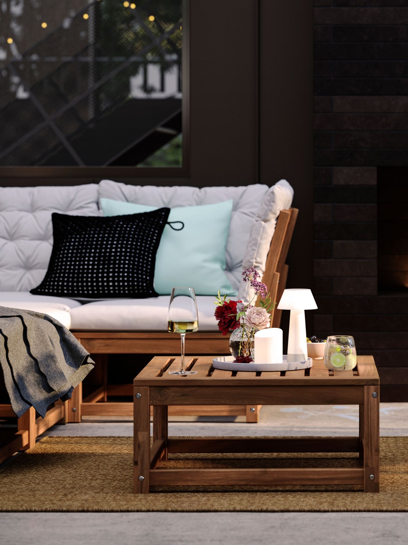 En NÄMMARÖ loungegrupp i trä med mjuka dynor och soffbord placerad vid en fasad i skugga.